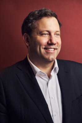 Portrait of a smiling man in a suit against a red background. 