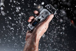 Electric shaver in hand under droplets of water 