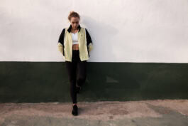 A person in a sporty outfit leans against a two-toned white and green wall, casting a shadow on a concrete floor. 