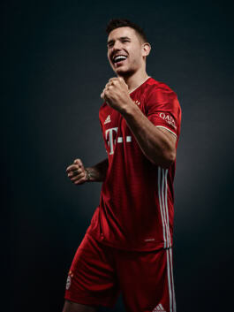 A person in a red sports uniform celebrates confidently against a dark background, displaying a joyful expression and clenched fists. 