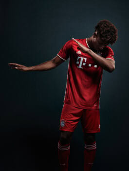 A person in a red soccer jersey performs a dab pose against a dark background. The jersey features Adidas and a star emblem. 
