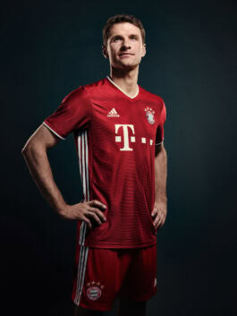 A person in a red football kit with Bayern Munich logos poses confidently against a dark background. 