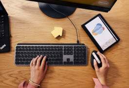 A person uses a computer keyboard and mouse on a wooden desk, next to a notepad labeled 
