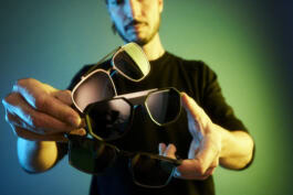 A person displays three pairs of Porsche Design sunglasses, with colorful lighting in the background, highlighting the stylish eyewear collection. 